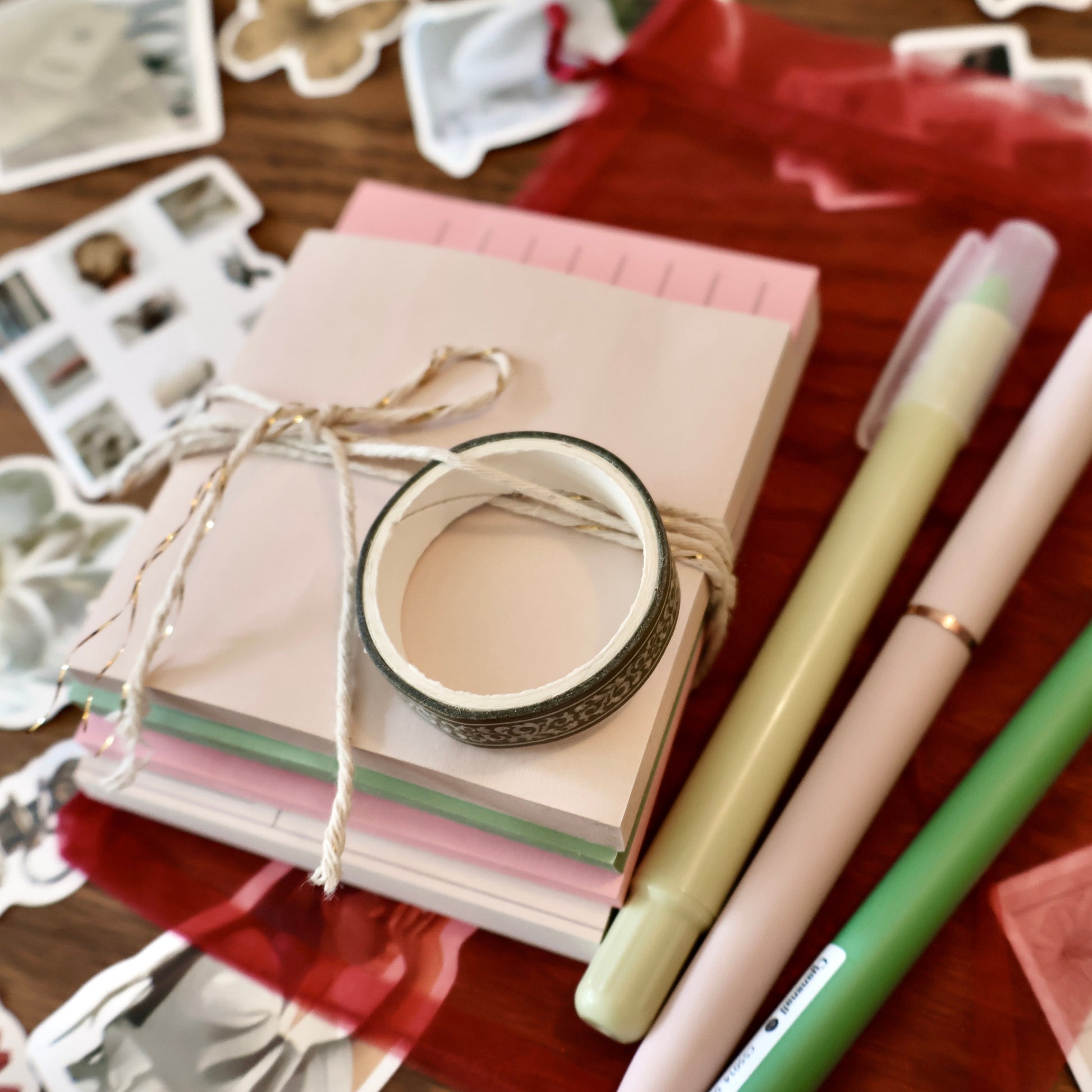Stationery items including pens, washi tape, and small note pads wrapped with twine on a wooden surface.