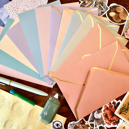 Collection of pastel-colored envelopes and stationery items on a wooden surface.