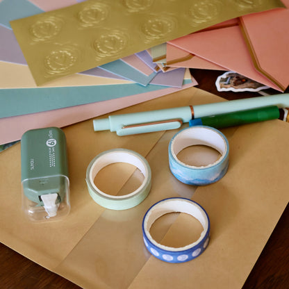 Assorted stationery items including paper, tape, and a pen on a wooden surface.