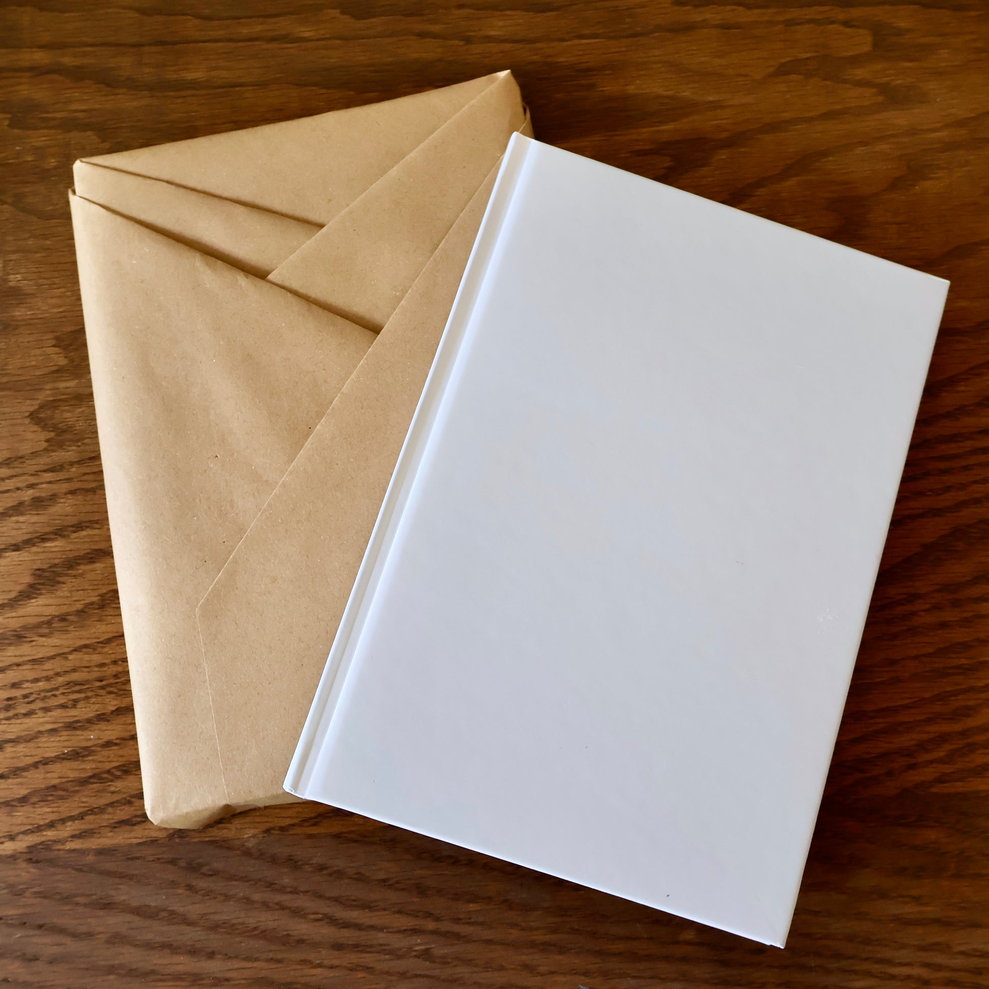 Kraft-wrapped journal and white notebook on a wooden surface.