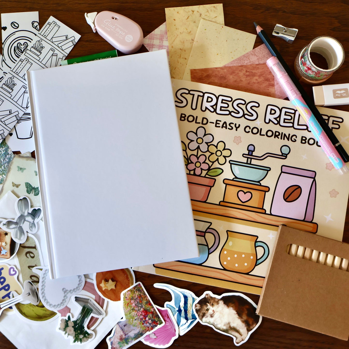 Coloring book titled 'Stress Relief' surrounded by stickers, a white journal, and stationery tools on a wooden surface