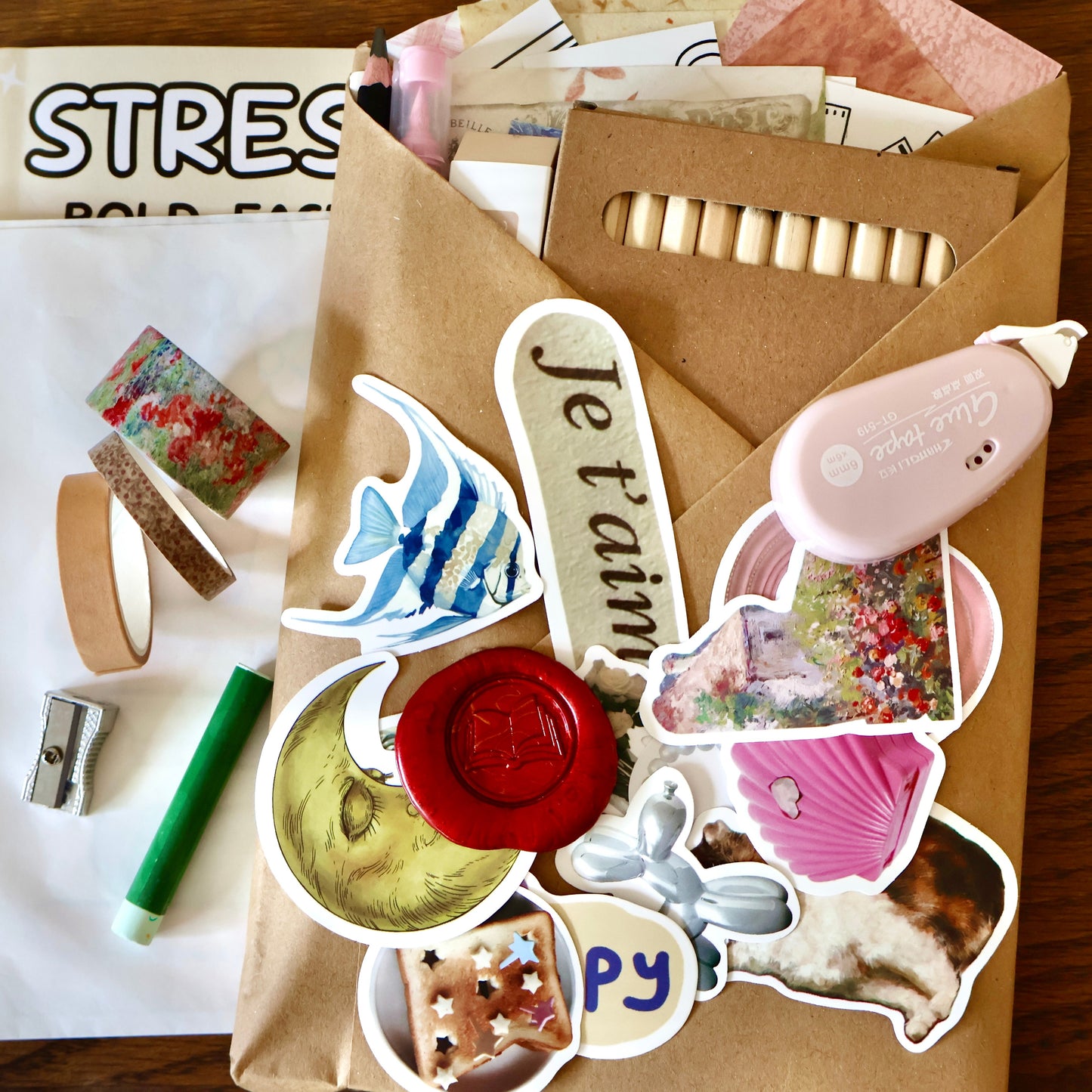 Sticker set with various designs and washi tapes on a wooden surface, with a kraft-wrapped journal.