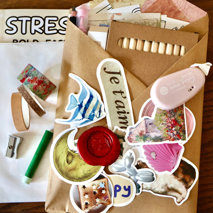 Sticker set with various designs and washi tapes on a wooden surface, with a kraft-wrapped journal.
