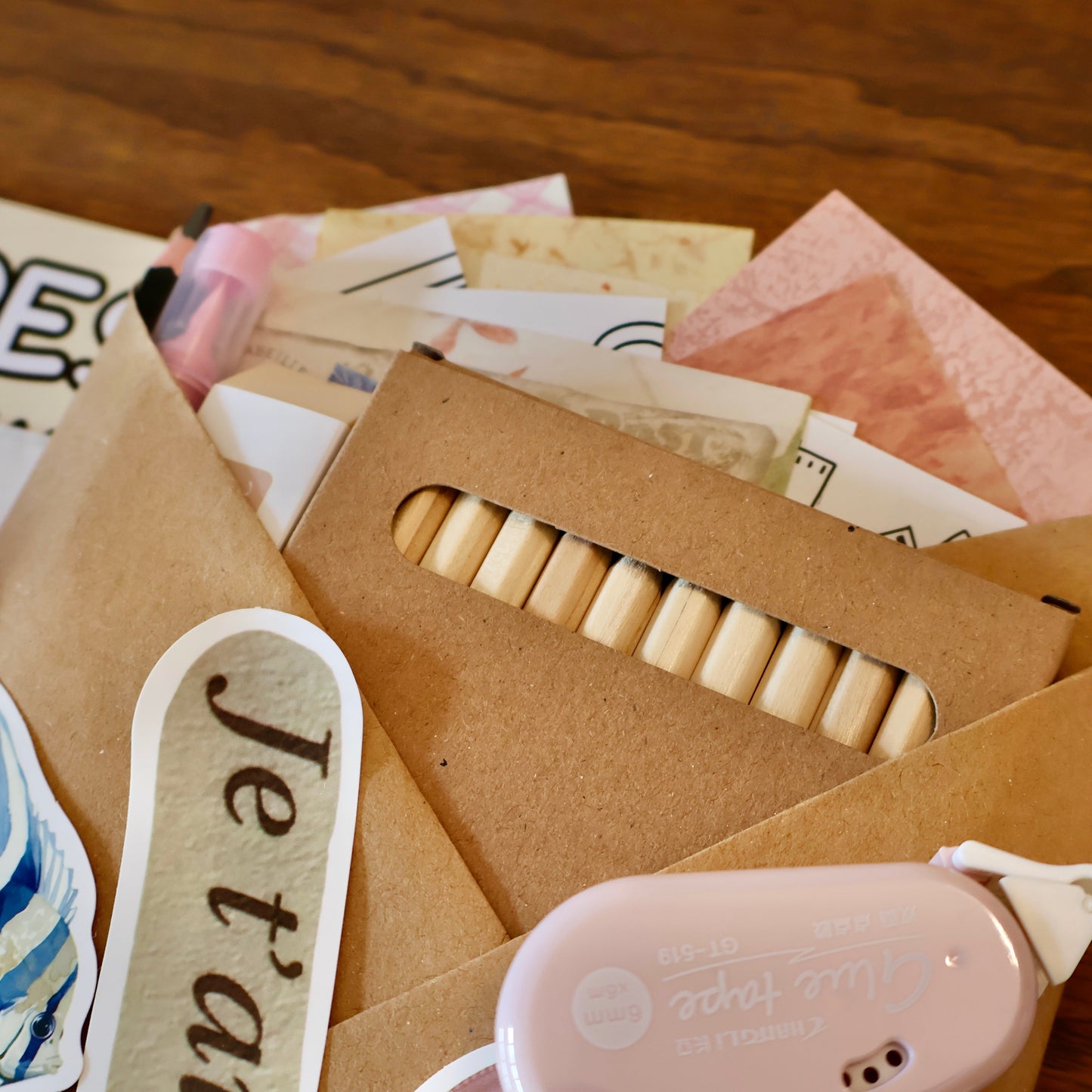 Collection of stationery items including papers, stickers, and a washi tape roll on a wooden surface.